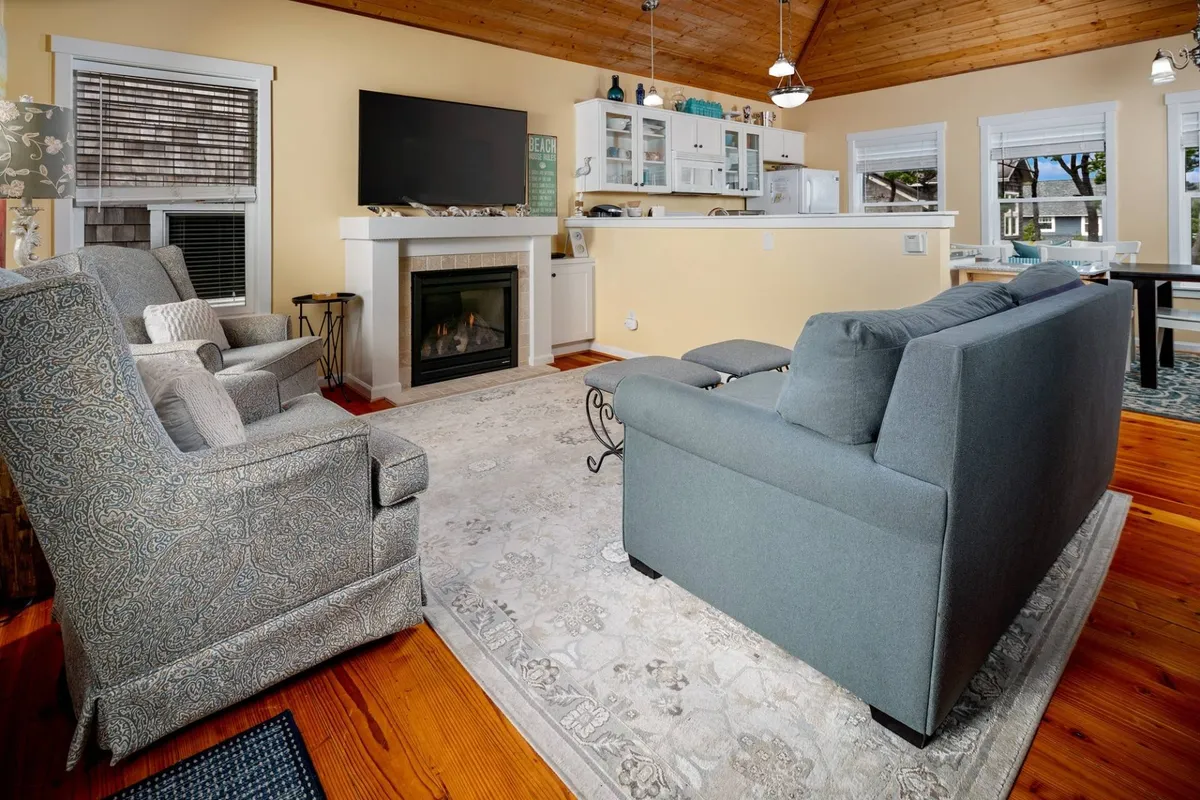 A warm, inviting living area centered around a gas fireplace, with plush sofas, a rug for playing games, and a television, all beneath a soaring wood-planked ceiling.