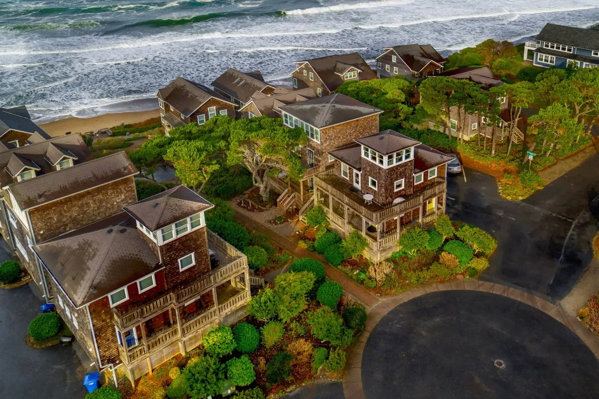 A scenic exterior view capturing rolling ocean waves, charming coastal homes, and lush greenery along the shoreline. The image evokes the tranquility and inspiration of Bella Beach, with plenty of sky overhead and a sense of openness and peace.