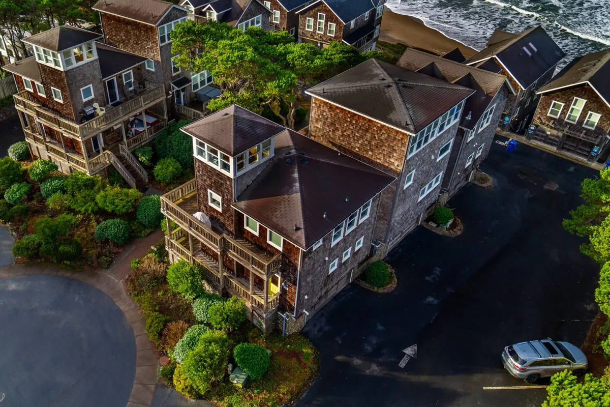 A picturesque exterior view of multiple Cape Cod-inspired homes nestled among lush greenery, with glimpses of ocean waves in the background. The scene is tranquil and inviting, exuding a sense of community as outdoor spaces are visible for family gatherings and relaxation.