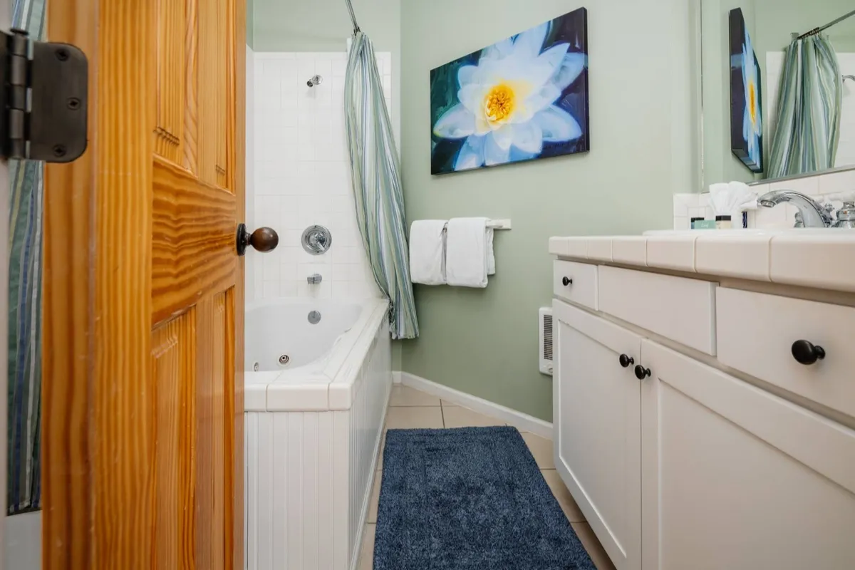 A tranquil bathroom scene featuring a whirlpool spa tub, flower artwork on the wall, and a vanity with a sink. The space is softly lit and exudes a spa-like atmosphere, perfect for relaxation and self-care routines.