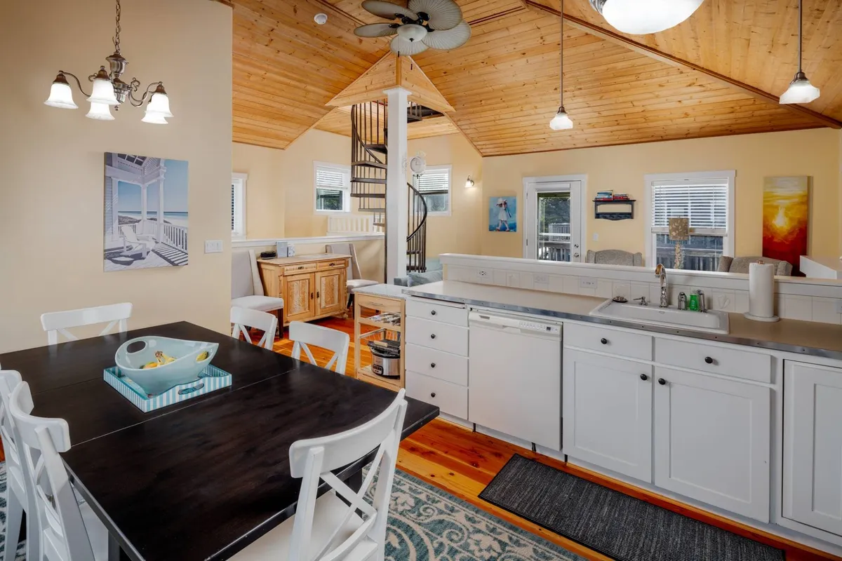 A welcoming main living area featuring a dining table, kitchen counter, and a striking spiral staircase. The bed beneath the staircase is subtly visible, turning a common area into a versatile nook for reading, sleeping, or lounging.