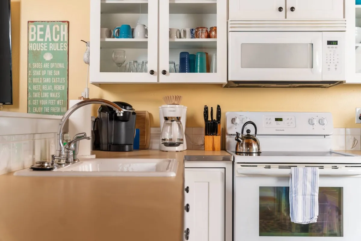 A bright, fully equipped kitchen with a stove, coffee maker, and ample counter space, set against windows that offer glimpses of surrounding greenery and, potentially, the ocean.