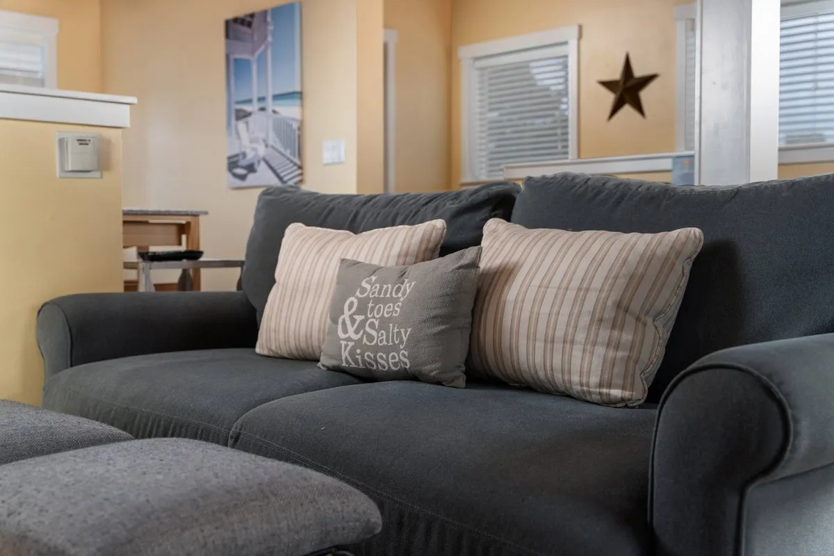 A cozy, stylish living space features a sofa with decorative pillows, wall art, and a star accent. Large windows allow sunset views, and the relaxed setup invites guests to unwind with movies or stories, capturing the spirit of togetherness after a day of exploring.